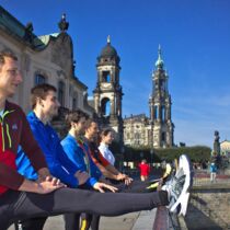 Laufgruppe dehnt Beinmuskulatur an Geländer